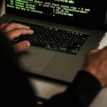 Crop anonymous male cyber spy hacking portable computer with codes on screen while sitting at table